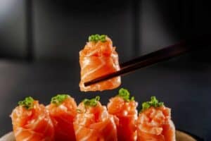 Salmon Jhow sushi on chopsticks in a black background. Closeup.